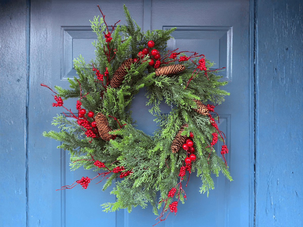 Vivid Christmas wreath featuring pine greenery, red berries, and pinecones hanging on a blue door.