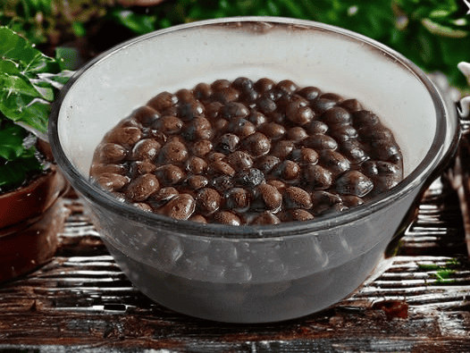 Fresh black beans soaking in a clear glass bowl, ideal for gardening or culinary use.